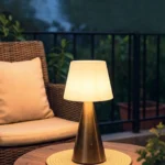 Neje Lighting | Aria Series: The Intersection of Cordless Innovation & Sculptural Artistry Aria gold cordless touch sensor lamp with a warm 3000K glow on an outdoor patio table, premium architectural lighting for modern Indian homes.